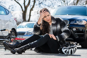 girl clutching her head on ground in front of car accident