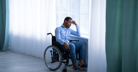 man in wheelchair looking sadly out window
